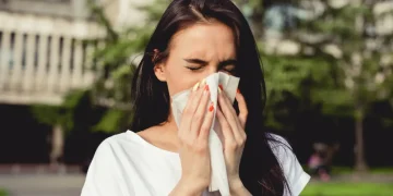Donna che starnutisce con un fazzoletto all’aperto, sintomi di allergia ai pollini